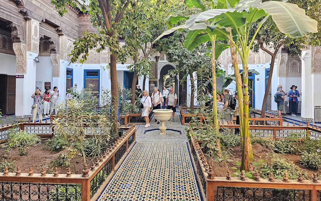 Visitors exploring the courtyard garden of Bahia Palace in Marrakech, Morocco.