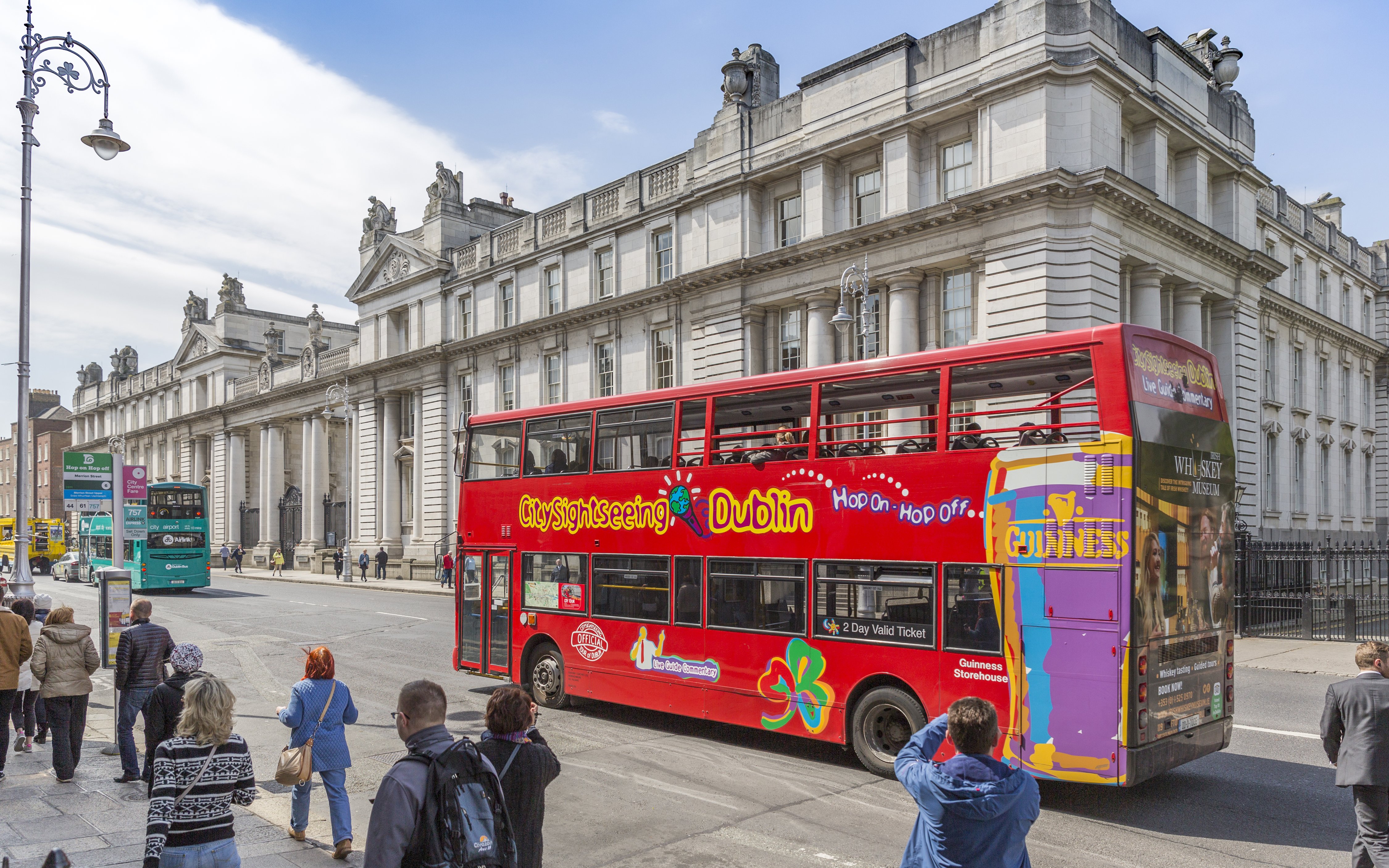 Open-top tour bus in Dublin passing historic government buildings.