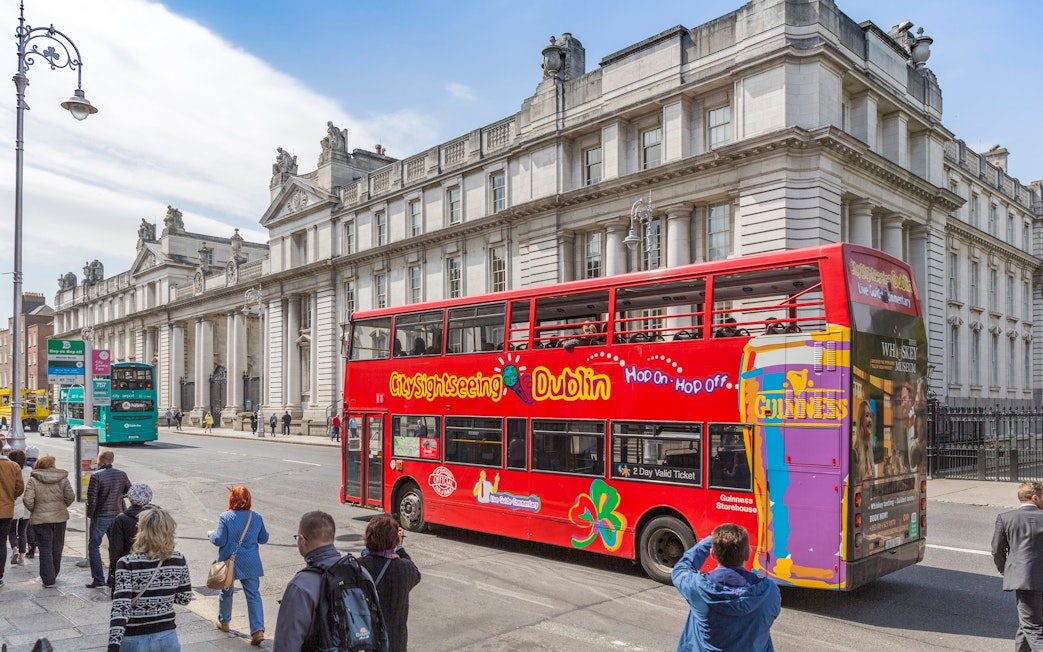 Open-top tour bus in Dublin passing historic government buildings.