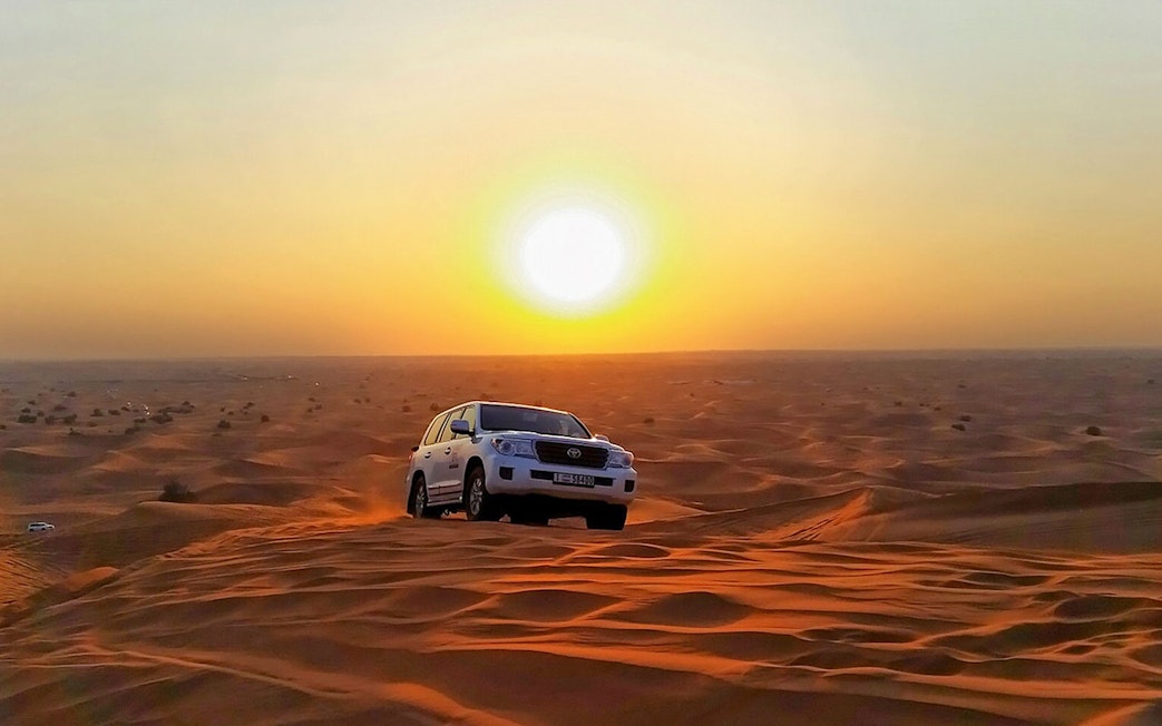 SUV driving over sand dunes at sunset during an evening safari adventure.