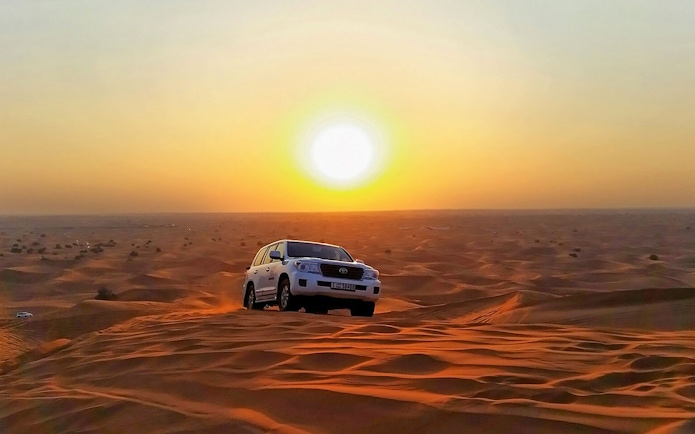 SUV driving over sand dunes at sunset during an evening safari adventure.