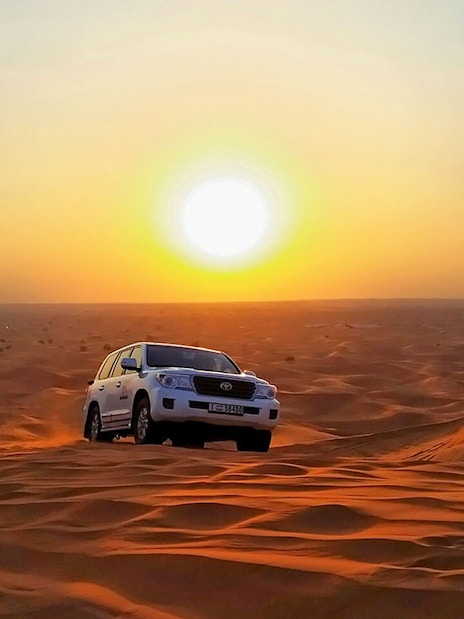 SUV driving over sand dunes at sunset during an evening safari adventure.