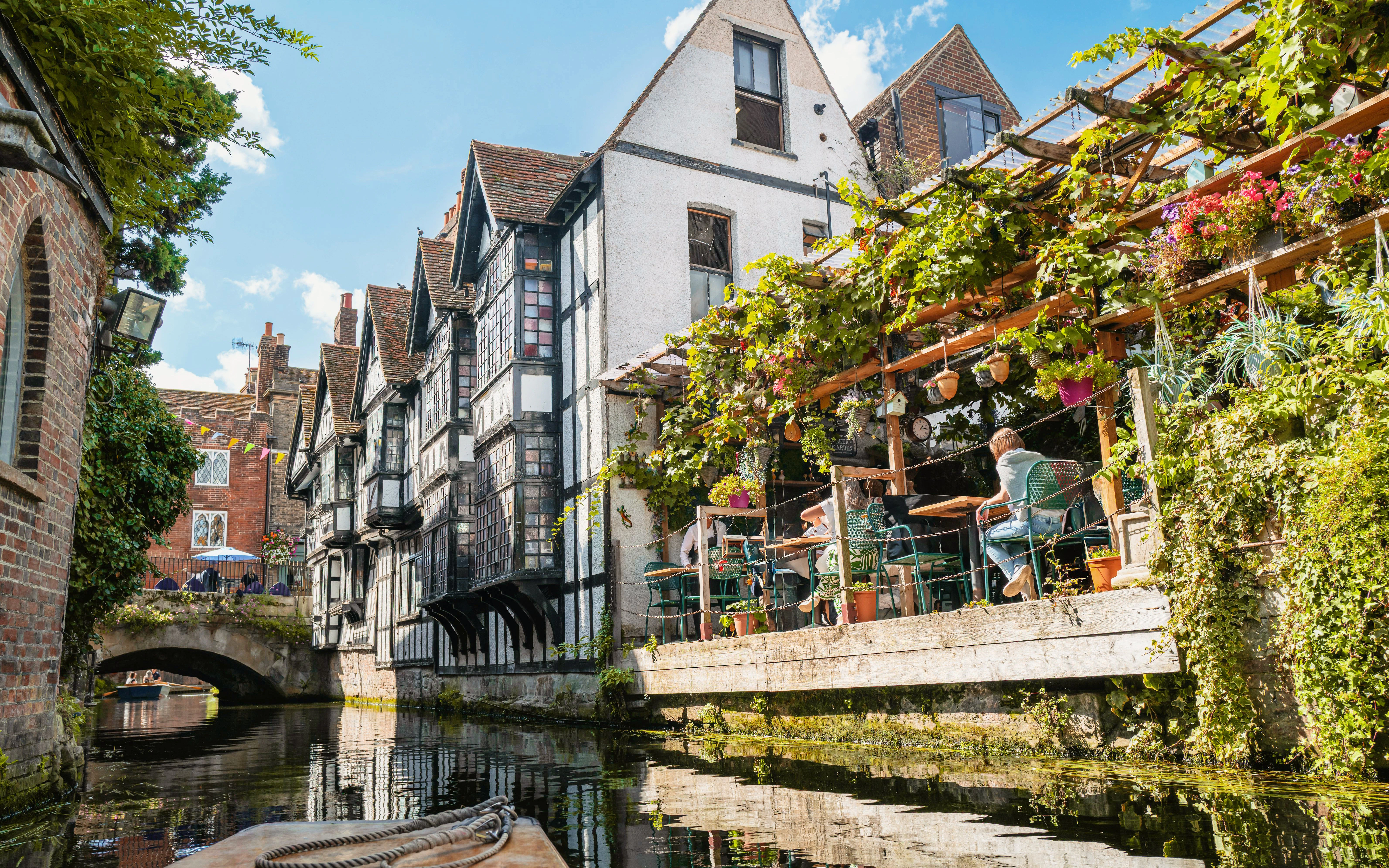 Timber-framed buildings along the River Stour in Canterbury, England, with outdoor seating.