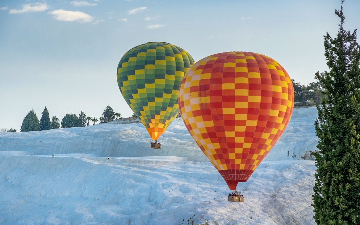 Hot air balloons over Pamukkale's travertine terraces in Turkey.