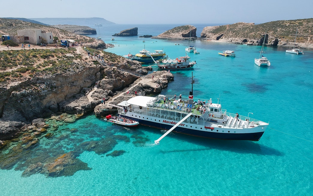 Cruise ship docked at Blue Lagoon, Malta with clear turquoise waters and rocky coastline.