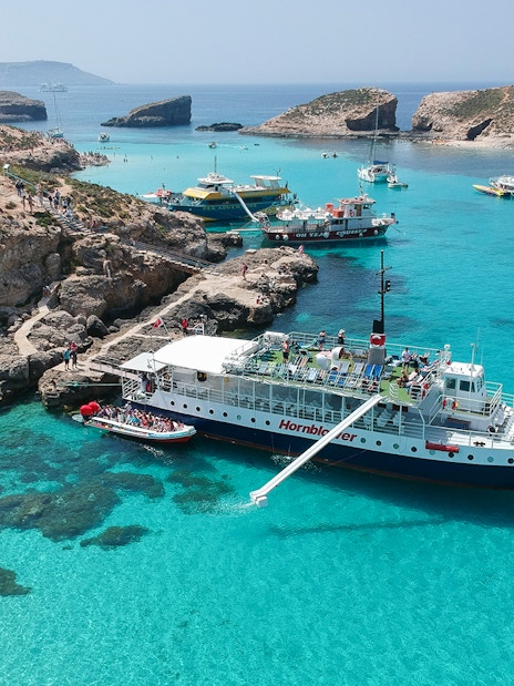 Cruise ship docked at Blue Lagoon, Malta with clear turquoise waters and rocky coastline.