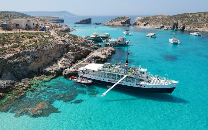 Cruise ship docked at Blue Lagoon, Malta with clear turquoise waters and rocky coastline.