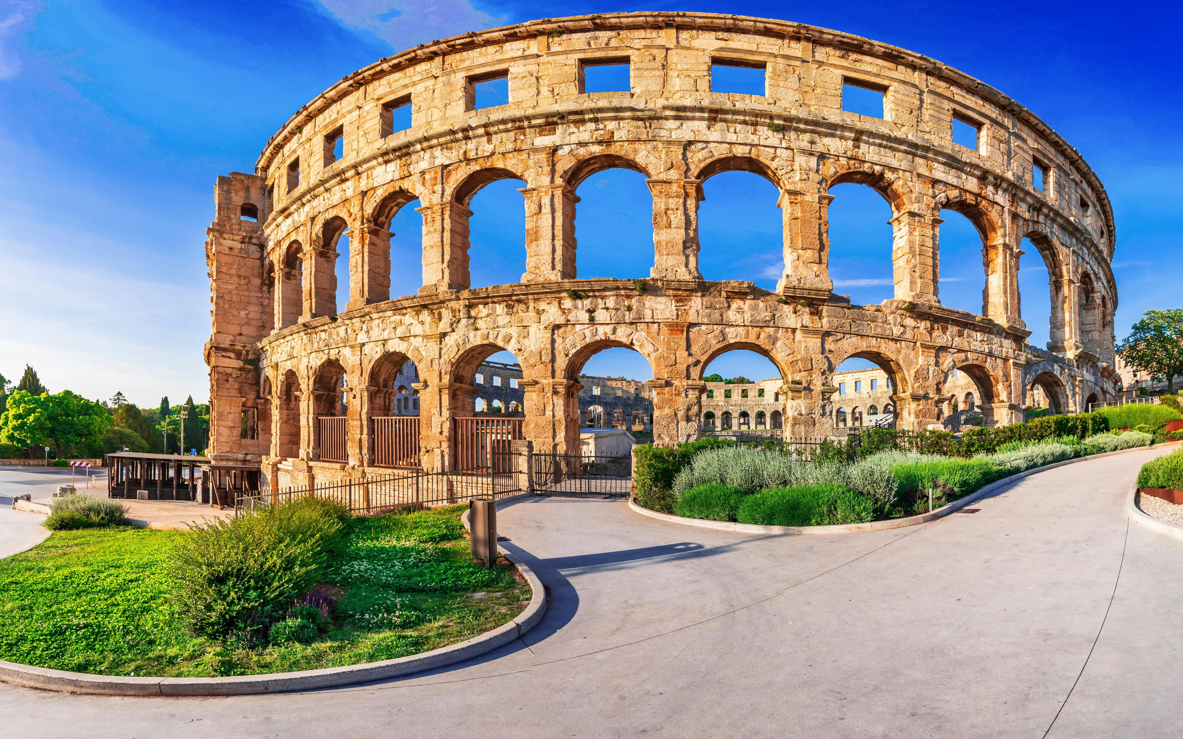 Pula Arena, ancient Roman amphitheater in Pula, Croatia, with stone arches and surrounding greenery.