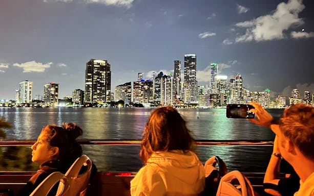 Passengers on Big Bus Miami Night Tour viewing illuminated Miami skyline.