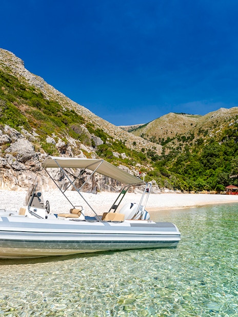 Boat on clear waters at Grama Bay, Albania, with rocky cliffs and lush greenery in the background.