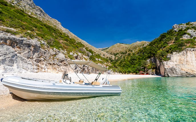 Boat on clear waters at Grama Bay, Albania, with rocky cliffs and lush greenery in the background.