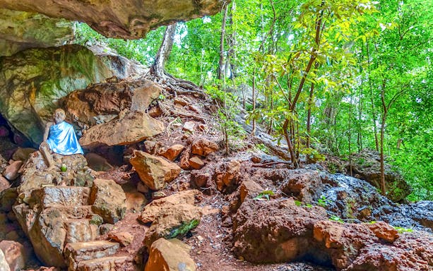 Monk statue in a rocky forest setting in Phuket, Thailand.