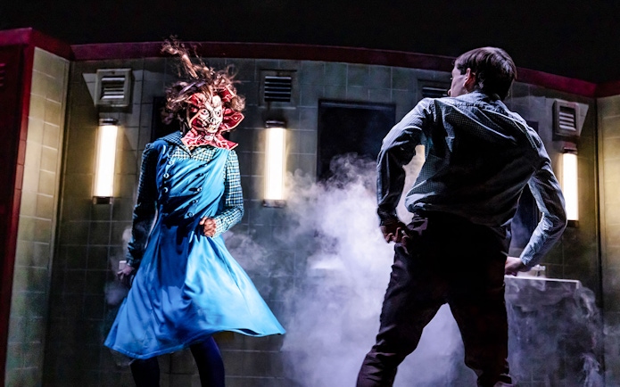 Character in blue dress with monster mask facing a person in a smoky room, Stranger Things theme.