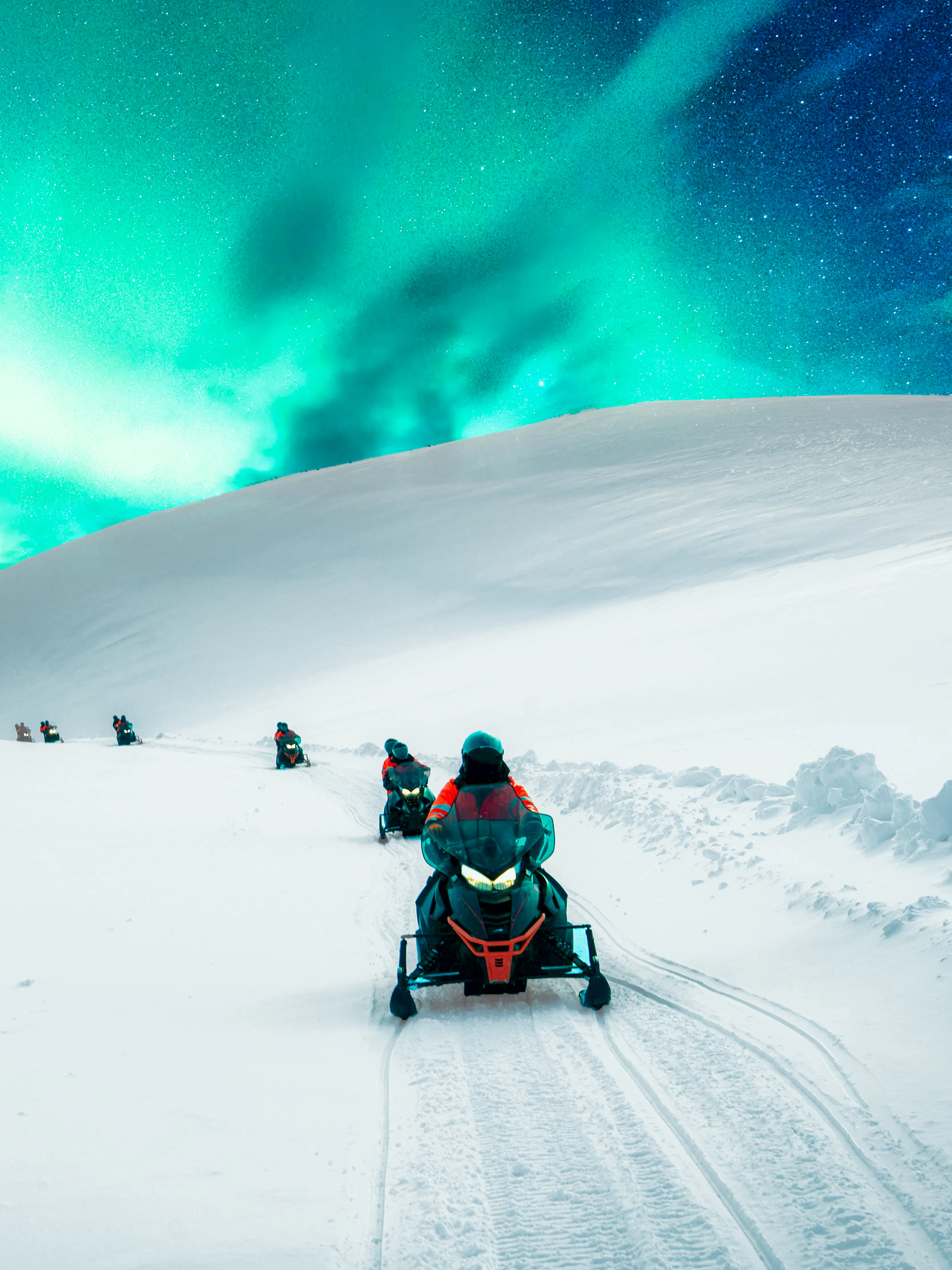 Snowmobiles on snowy mountain trail under aurora borealis in winter.
