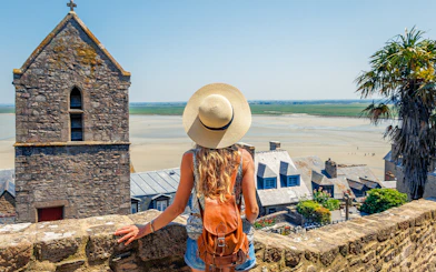 Woman with backpack overlooking Mont Saint Michel in Normandy, France.