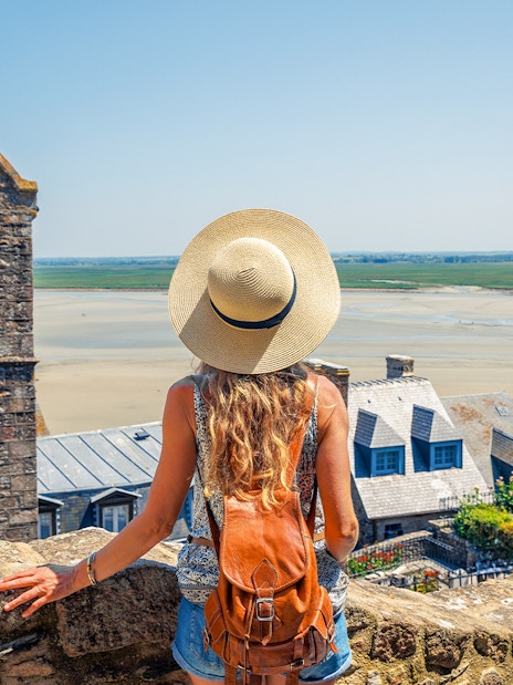 Woman with backpack overlooking Mont Saint Michel in Normandy, France.