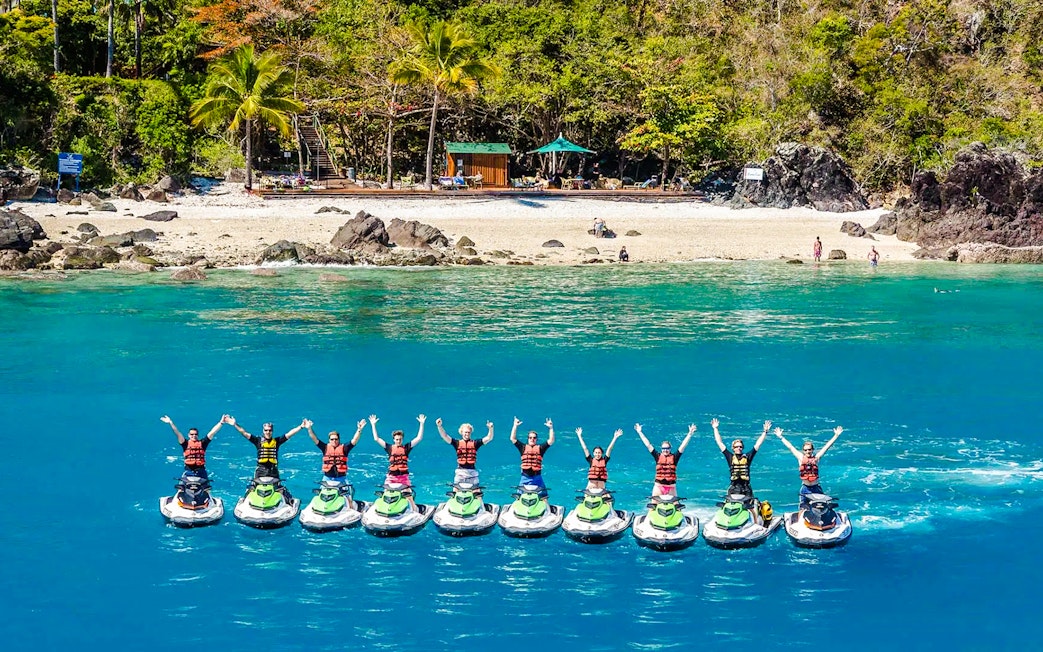Tourists on jetskis in formation near Whitsundays beach, aerial view.