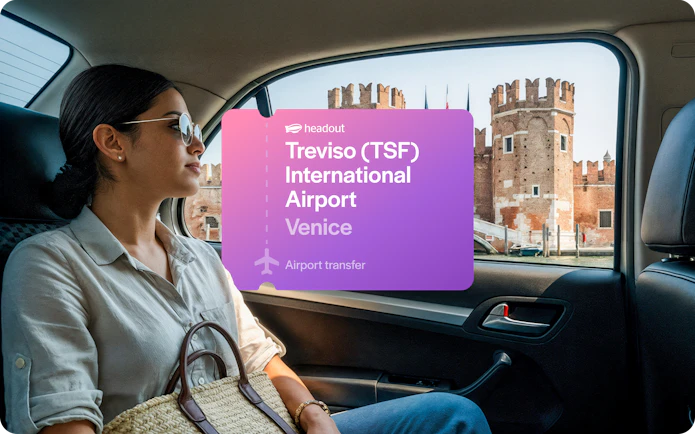 Woman in car with view of Venetian architecture, Treviso Airport transfer sign.