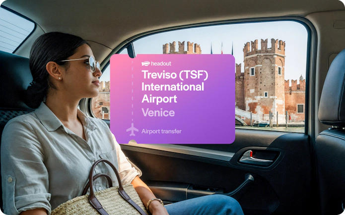 Woman in car with view of Venetian architecture, Treviso Airport transfer sign.