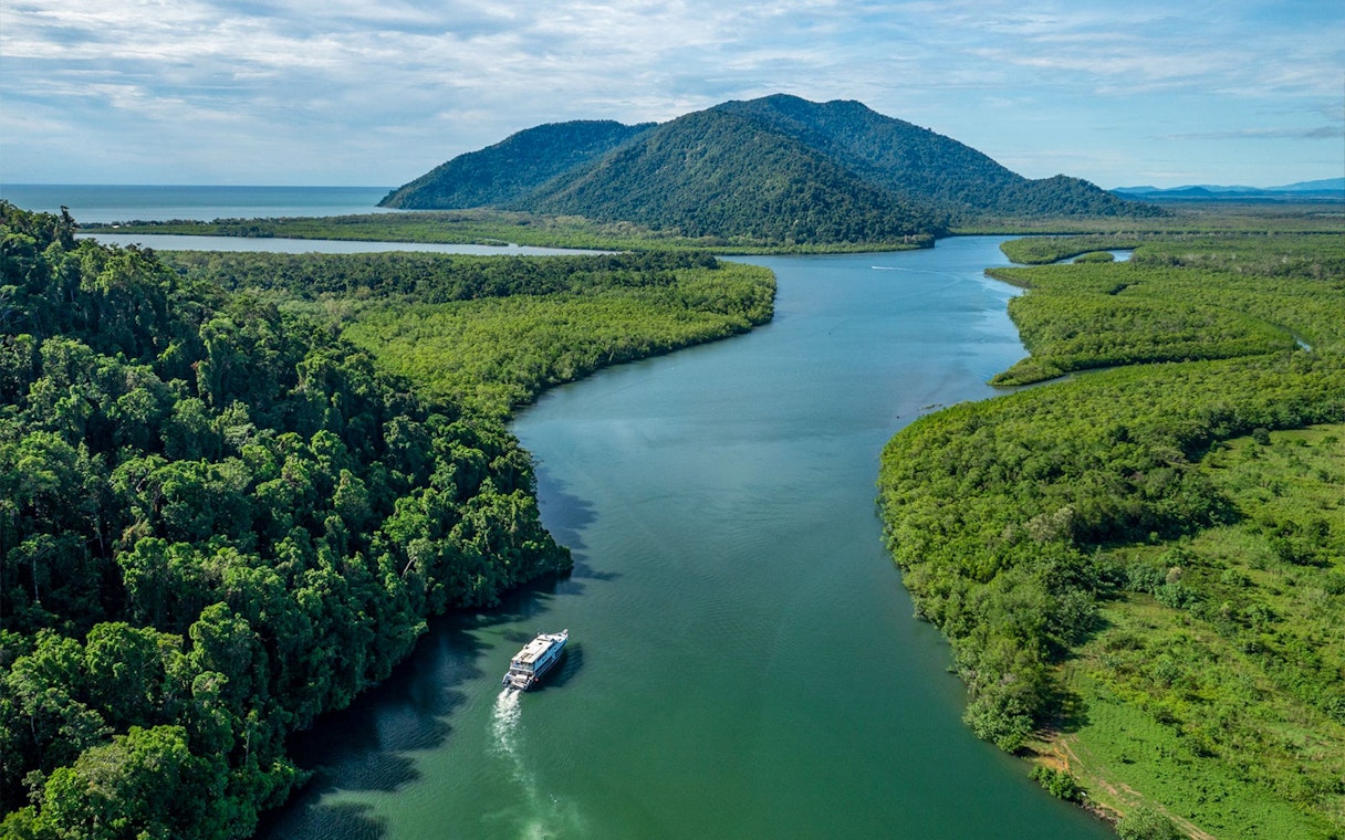 Boat cruising through rainforest river near Frankland Islands, Australia.