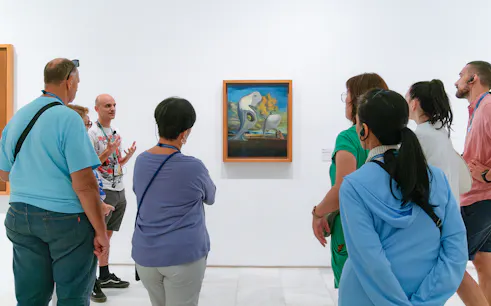 Visitors on a guided tour at Prado Museum viewing surrealist painting.