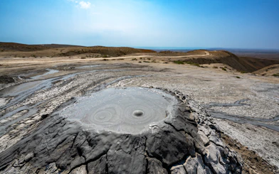 Mud volcano with cracked earth in arid landscape beneath clear sky.