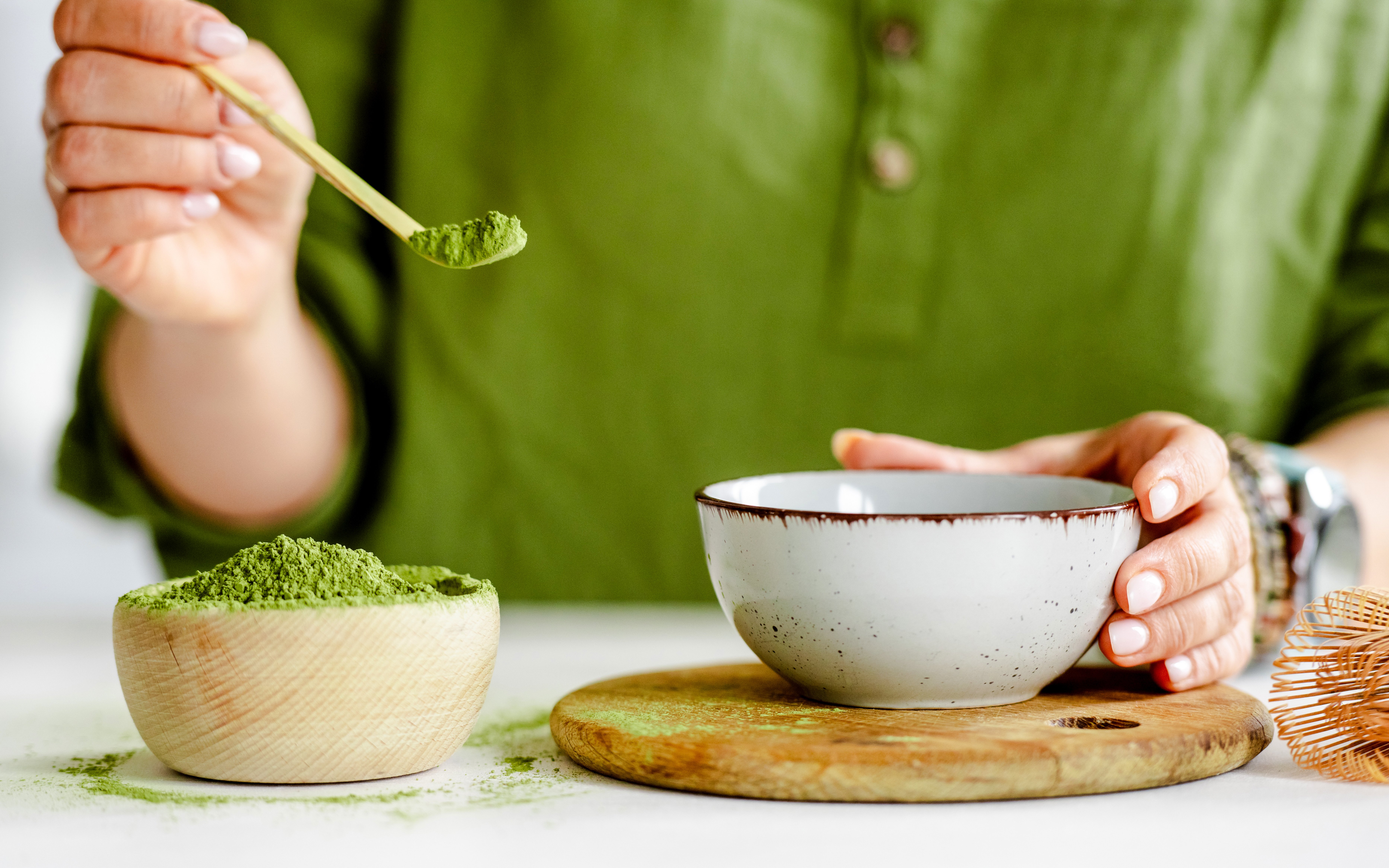 Person preparing matcha tea with a bamboo scoop and ceramic bowl.