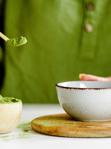 Person preparing matcha tea with a bamboo scoop and ceramic bowl.