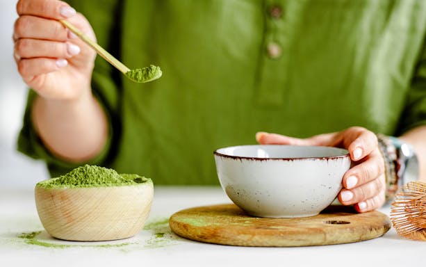 Person preparing matcha tea with a bamboo scoop and ceramic bowl.