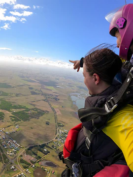 Skydivers tandem jumping over Melbourne countryside, pointing at landscape below.
