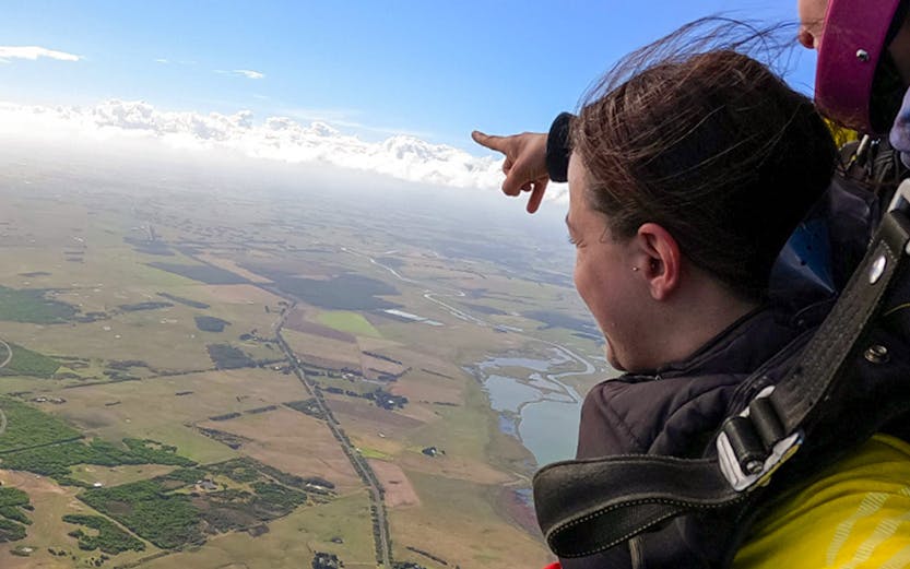 Skydivers tandem jumping over Melbourne countryside, pointing at landscape below.