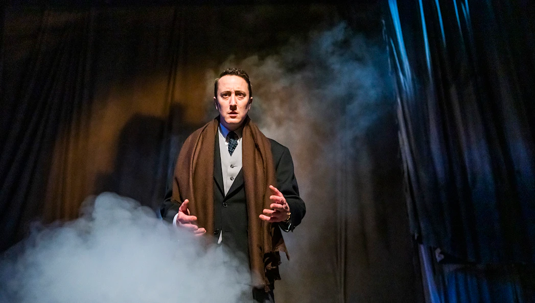 Actor performing in "The Woman in Black" play with dramatic lighting and fog.