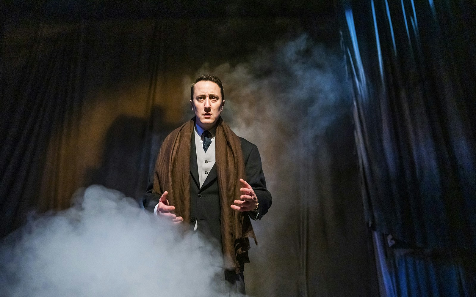 Actor performing in "The Woman in Black" play with dramatic lighting and fog.