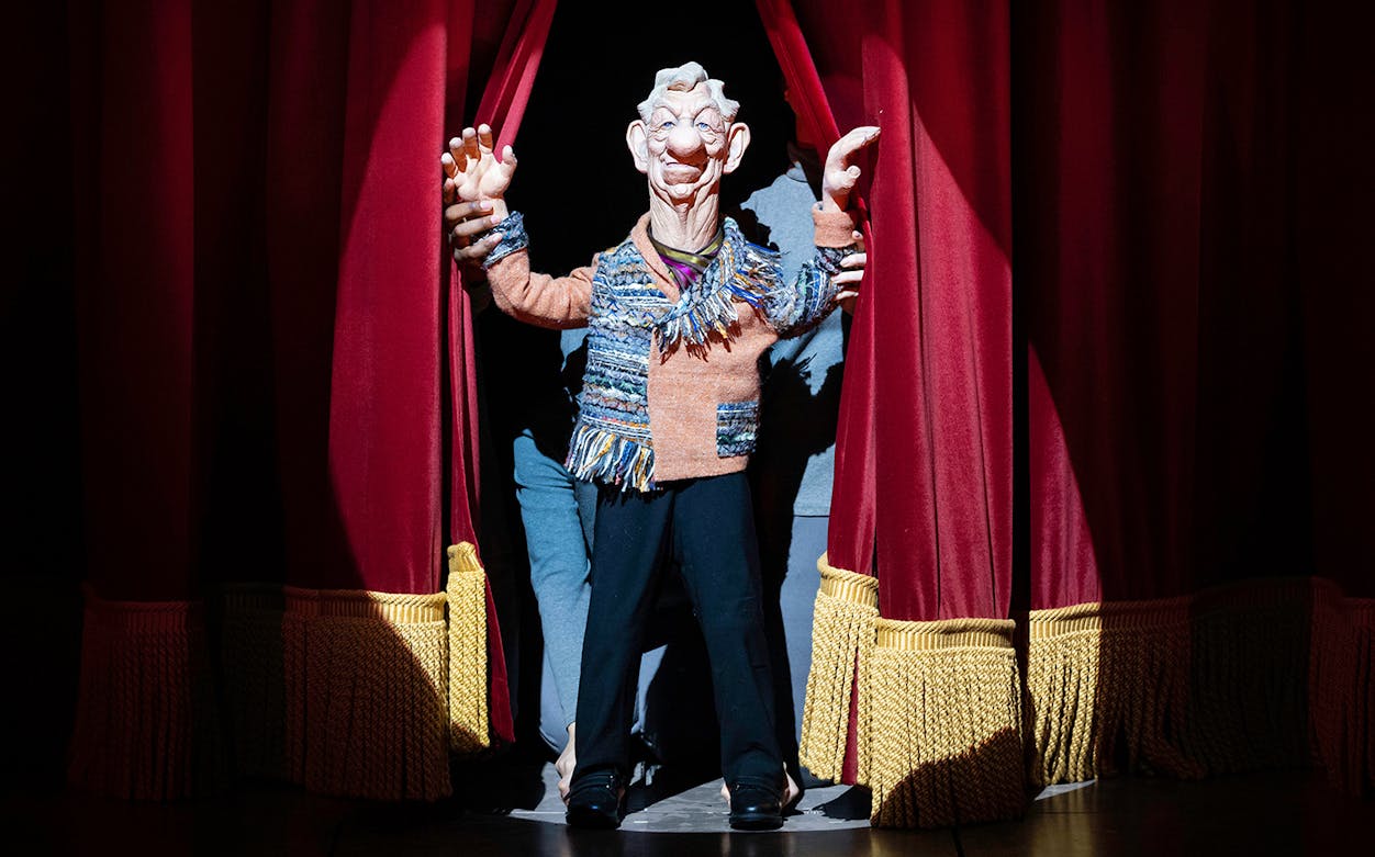 Puppet character on stage behind red curtains in "Idiots Assemble: Spitting Image the Musical.