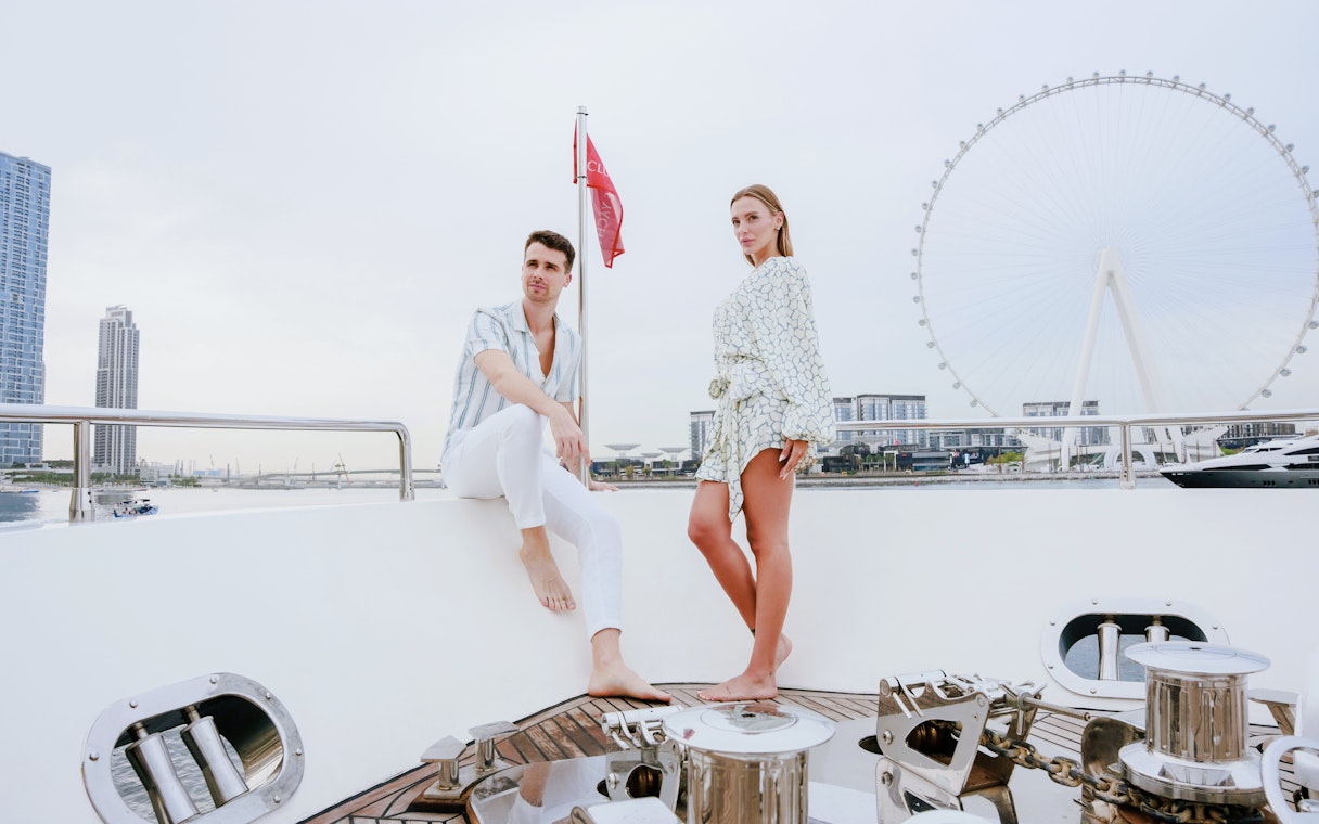 Couple on a luxury yacht with Dubai skyline and Ferris wheel in the background.