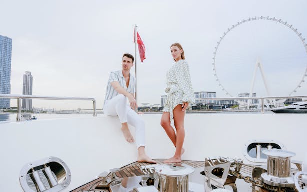 Couple on a luxury yacht with Dubai skyline and Ferris wheel in the background.