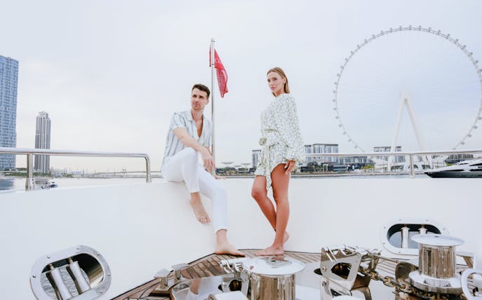 Couple on a luxury yacht with Dubai skyline and Ferris wheel in the background.