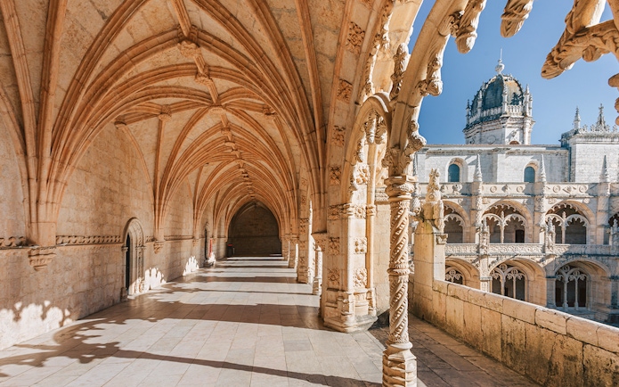 Jerónimos Monastery cloister with ornate arches and sunlight, Lisbon, Portugal.