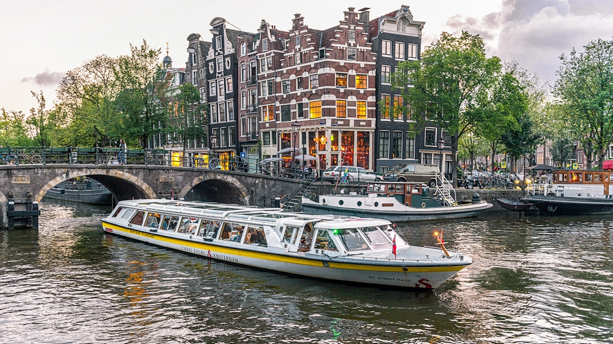 Canal boat cruising past historic buildings and bridge in Amsterdam city center.