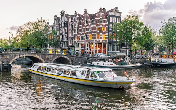 Canal boat cruising past historic buildings and bridge in Amsterdam city center.