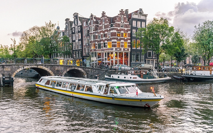 Canal boat cruising past historic buildings and bridge in Amsterdam city center.