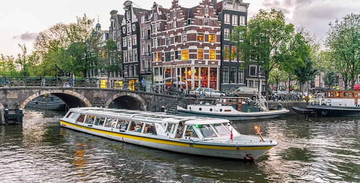 Canal boat cruising past historic buildings and bridge in Amsterdam city center.