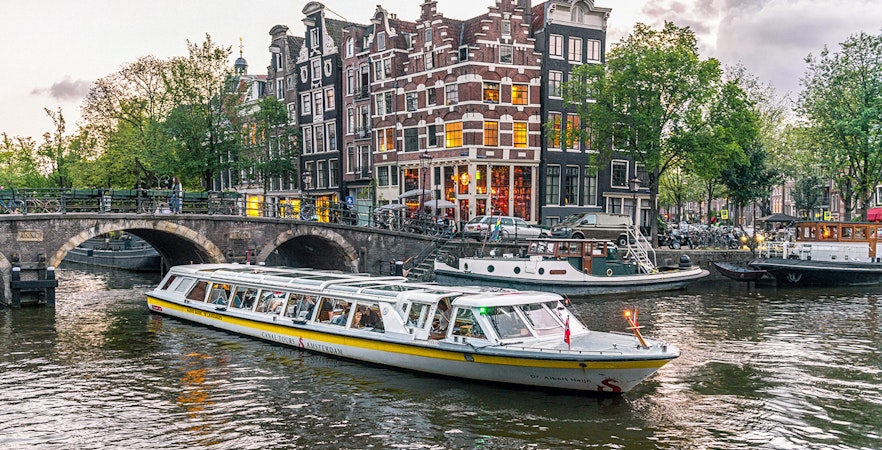 Canal boat cruising past historic buildings and bridge in Amsterdam city center.