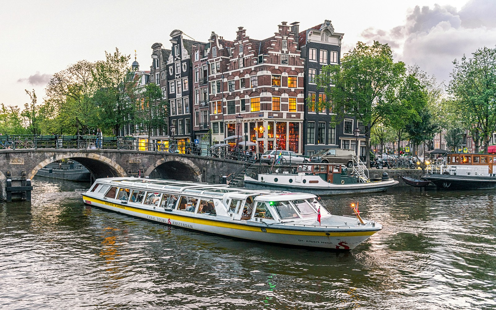 Canal boat cruising past historic buildings and bridge in Amsterdam city center.