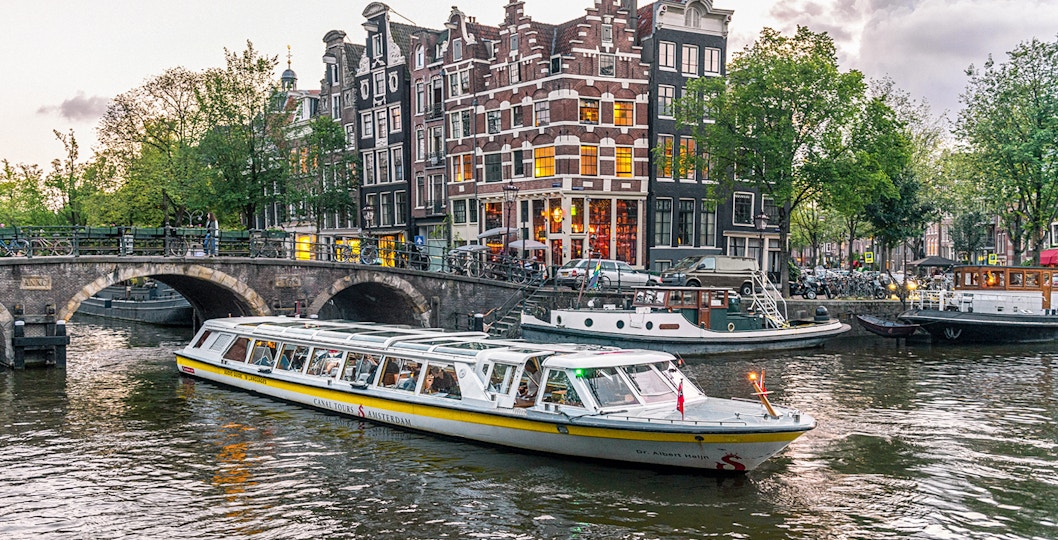 Canal boat cruising past historic buildings and bridge in Amsterdam city center.