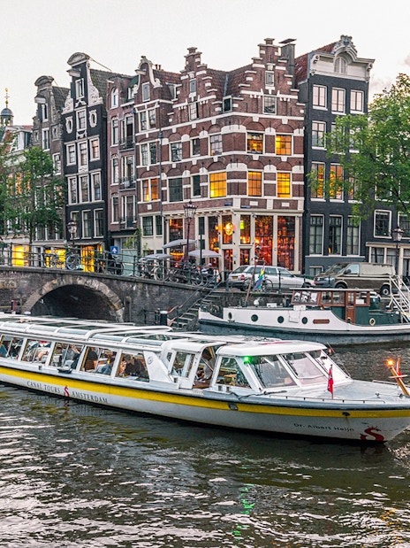 Canal boat cruising past historic buildings and bridge in Amsterdam city center.