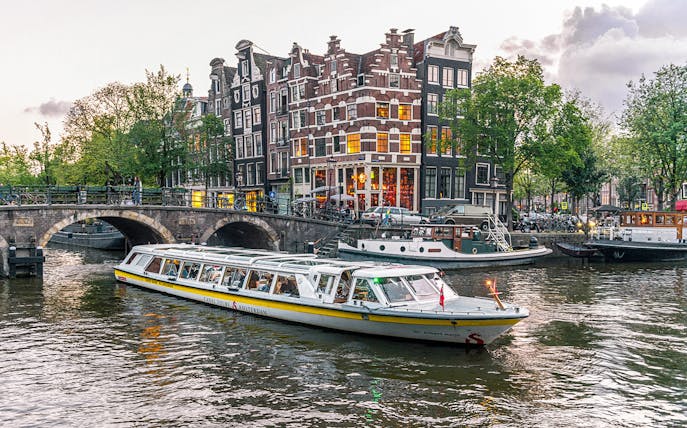 Canal boat cruising past historic buildings and bridge in Amsterdam city center.