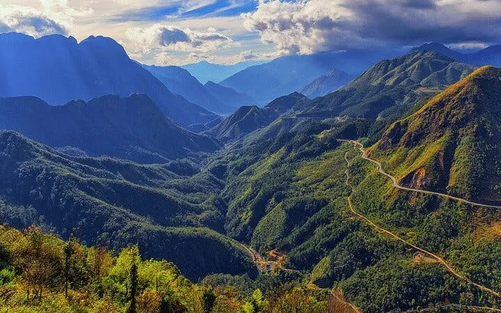 Mountainous landscape in Sapa with winding road leading to Heaven's Gate under a cloudy sky.