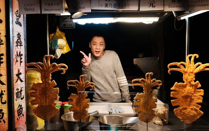 Vendor at Taipei street food stall with fried squid skewers on display.