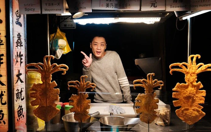 Vendor at Taipei street food stall with fried squid skewers on display.